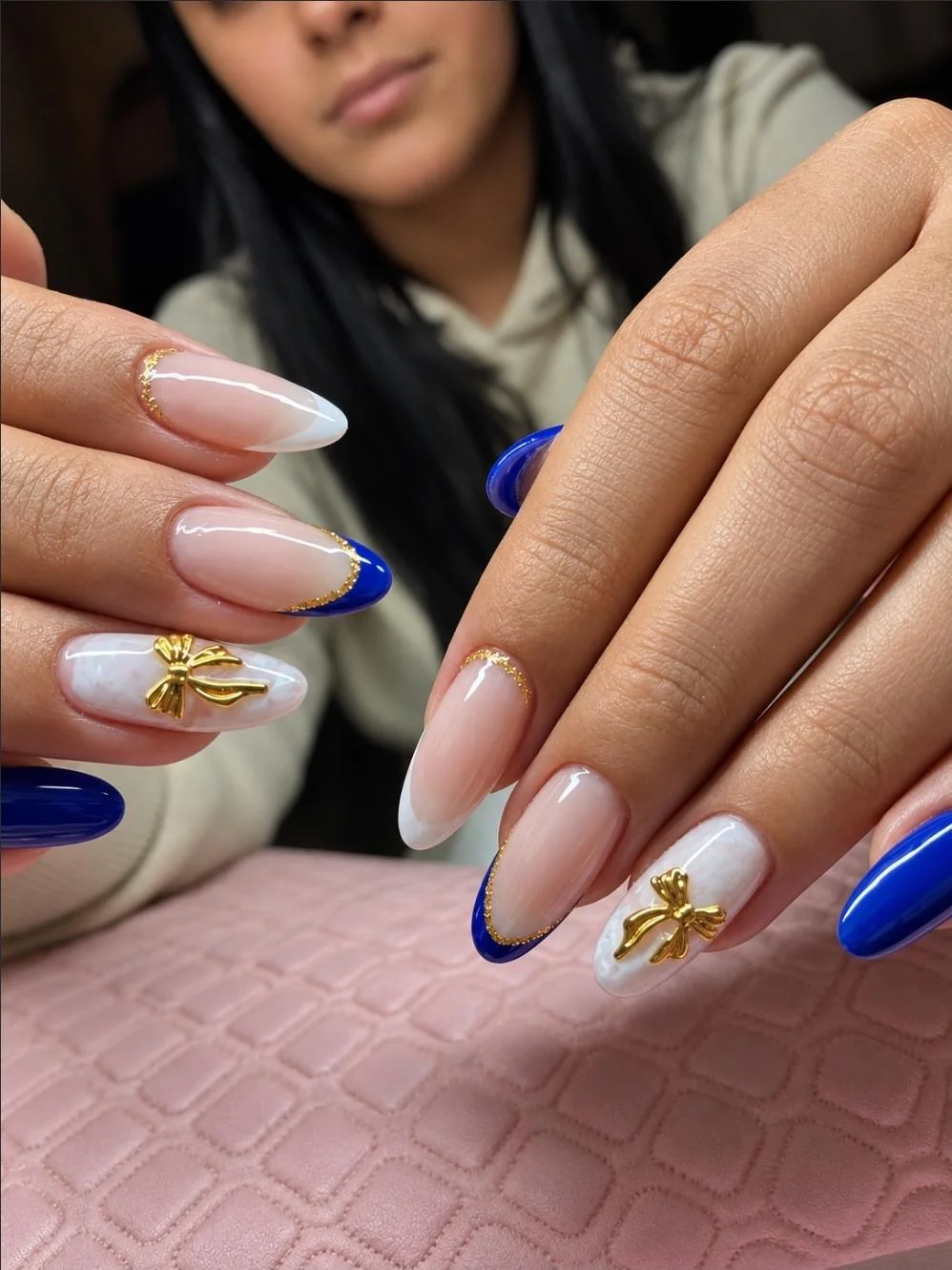 Unhas amêndoa com nail art azul royal e laços dourados