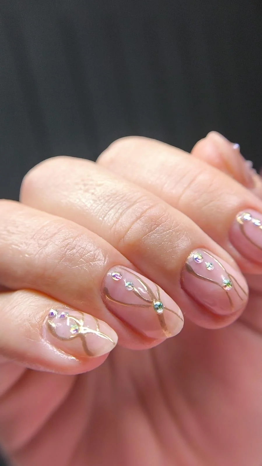 Unhas com nail art em linhas douradas e pedrinhas iridescentes